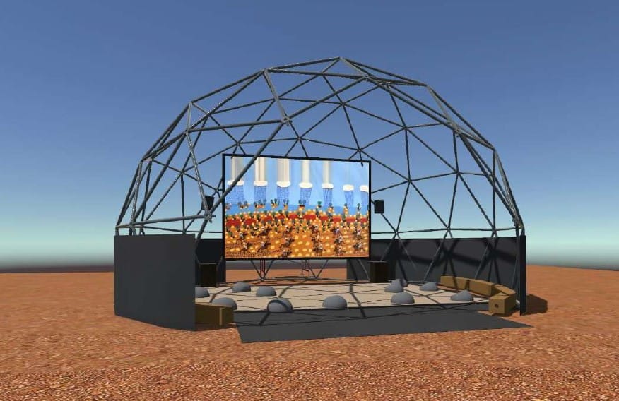 Geodesic dome structure with a large screen displaying artwork; surrounded by seating, set on a barren landscape under a clear blue sky.