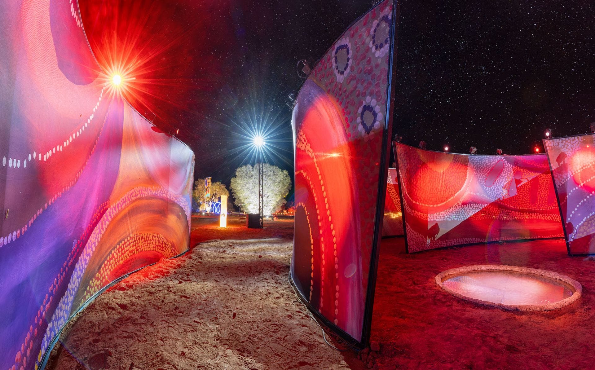 Bright, colorful panels with dot patterns are illuminated in a desert night setting, with stars visible in the sky and vivid lighting effects.