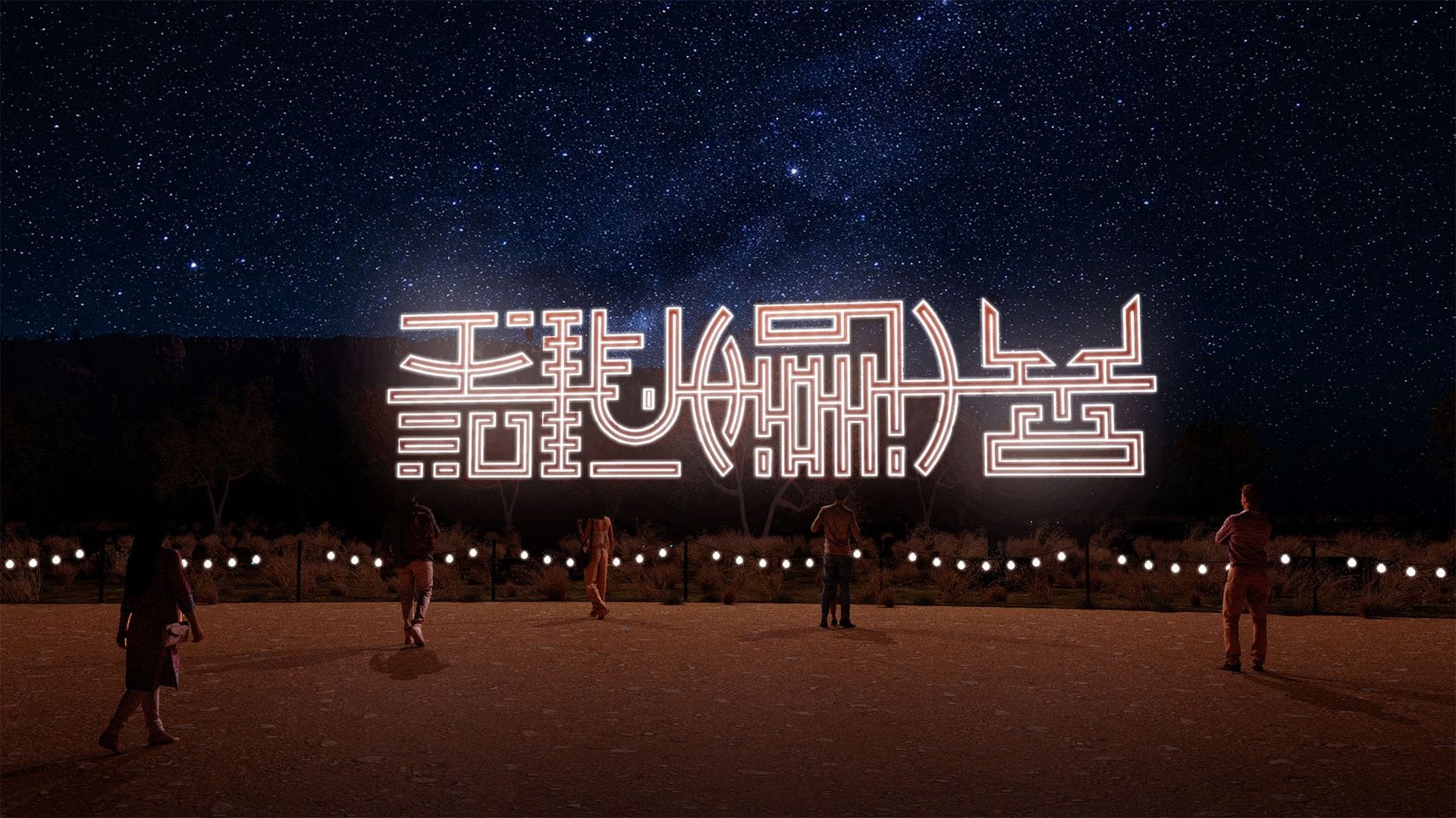 People admire large, glowing neon characters set against a starry night sky in a desert landscape.